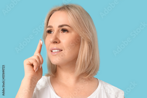 Beautiful mature happy woman applying cream on blue background