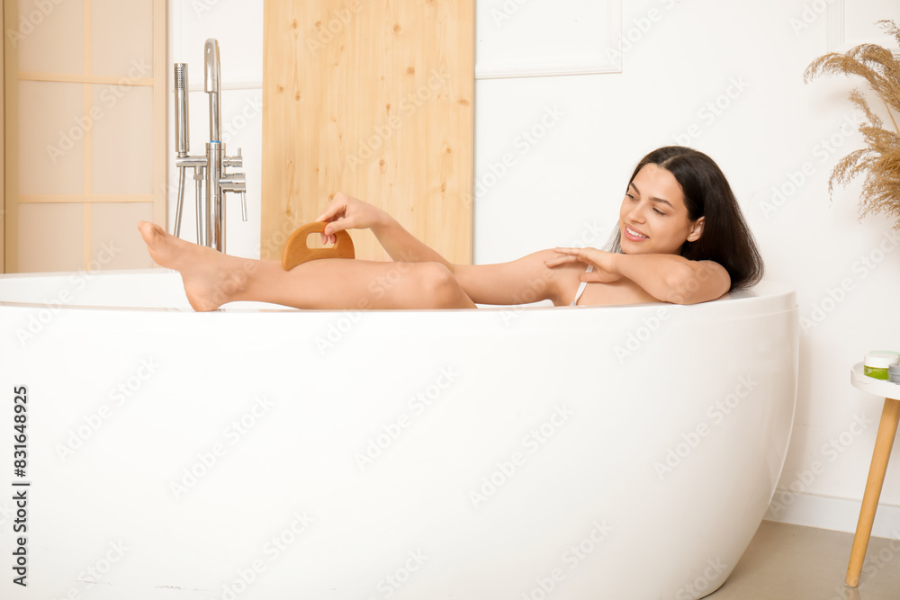 Young woman massaging her leg with wooden scraper in bathtub at home Young woman massaging her leg with wooden scraper in bathtub at home