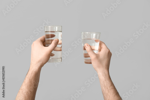 Male hands with glasses of clean water on grey background