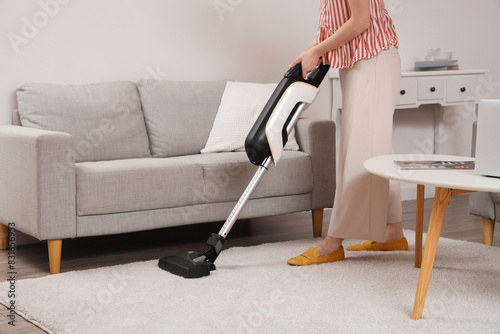 Young woman cleaning carpet with cordless stick vacuum cleaner in living room photo
