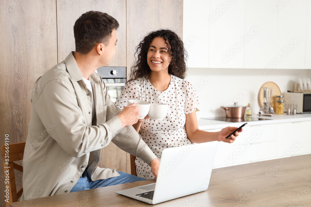 Young loving couple with cups of coffee and mobile phone in kitchen
