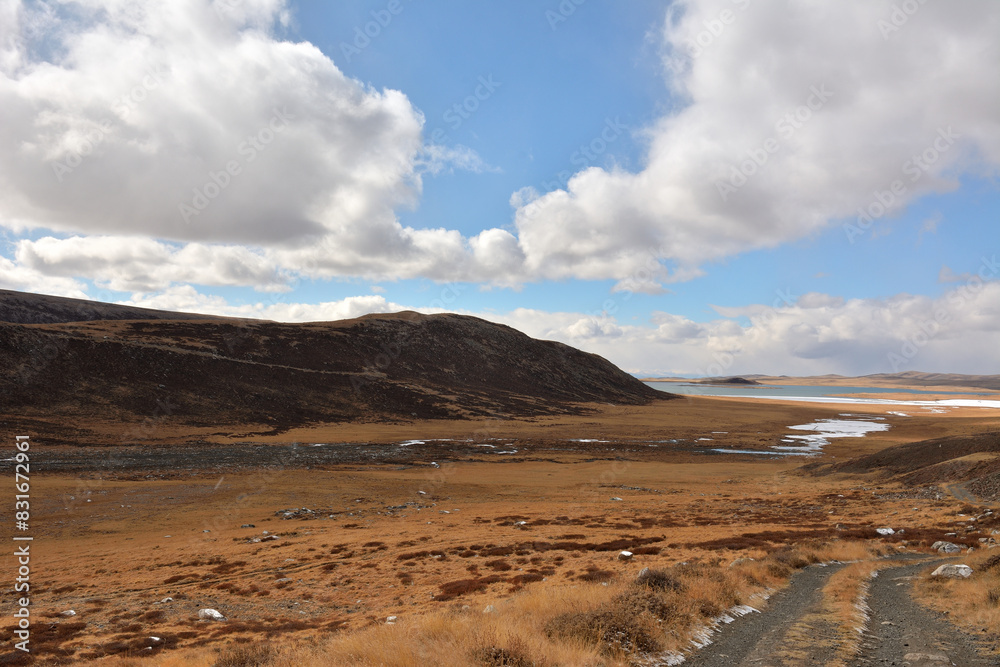 A winding gravel road descends the hill into a picturesque valley with a huge lake on a sunny autumn day. A winding gravel road descends the hill into a picturesque valley with a huge lake on a sunny autumn day.