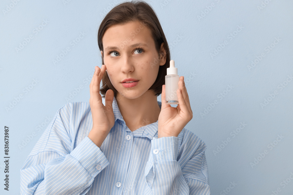 Beautiful young woman with acne problem and bottle of skincare serum on blue background Beautiful young woman with acne problem and bottle of skincare serum on blue background