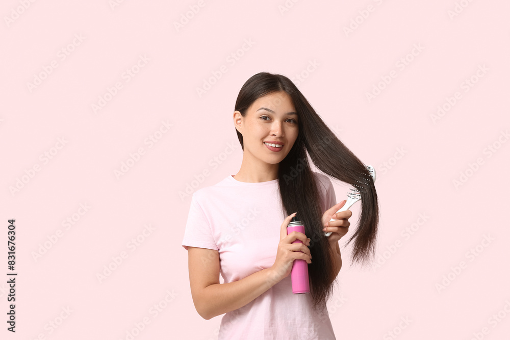 Beautiful young happy woman with brush applying hair spray on pink background Beautiful young happy woman with brush applying hair spray on pink background