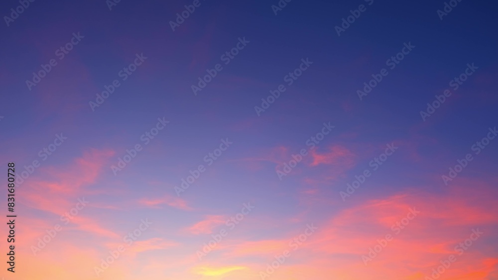 Fototapeta premium A vibrant sunset sky transitioning from deep blue at the top to soft pinks and purples. Wispy clouds are illuminated with warm hues, creating a striking and serene scene. Sunset sky background. 