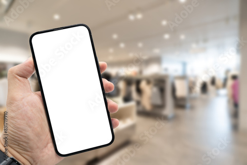 Hand holding blank screen smartphone for copy space on blurred clothing store. e-commerce app shopping mockup. social media, payment and shopping online concept. fashion and technology.