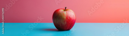 A vibrant red apple placed on a blue surface against a pink background, captured in a minimalist and colorful setting.