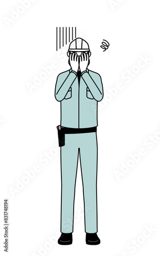 Man in helmet and workwear covering his face in depression.