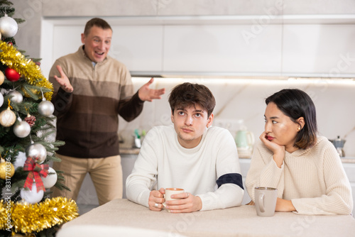 Adult man during family quarrel with young guy and young woman in kitchen at home