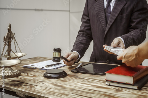 A businessman in a formal suit signs a contract, hands close up, suggesting possible bribery, at a wooden desk with legal documents, scales, and a wooden gavel representing legislation.