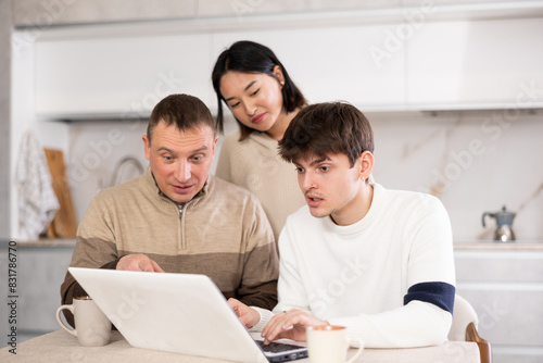 Adult man and couple of young guy and young woman using laptop in kitchen at home © JackF
