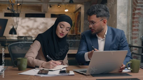 Two business colleagues co-workers talk discuss corporate work at office cafe multiracial male female employees Indian man muslim woman in hijab diverse businesswoman businessman write tasks laptop photo