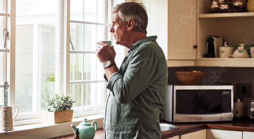 Window, tea and mature man in kitchen thinking for memory, reflection or idea at home in morning. Dreaming, reflection and male person drinking cup of coffee by glass door for brainstorming at house.