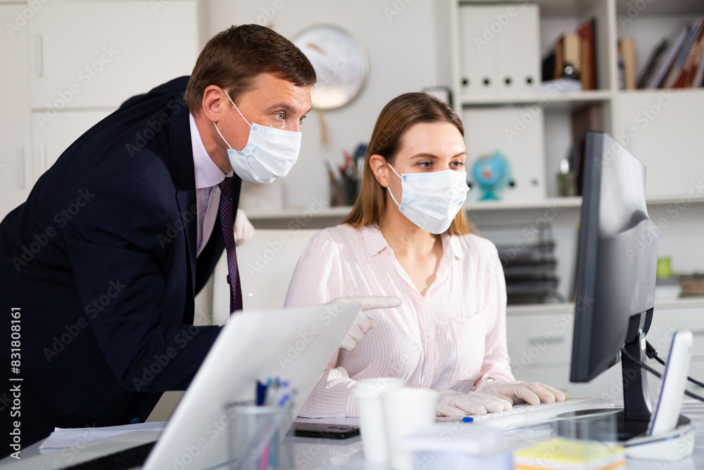 Fototapeta premium Portrait of busy entrepreneur in medical face mask and latex gloves working with female coworker in office. Concept of precautions and social distancing in coronavirus pandemic..