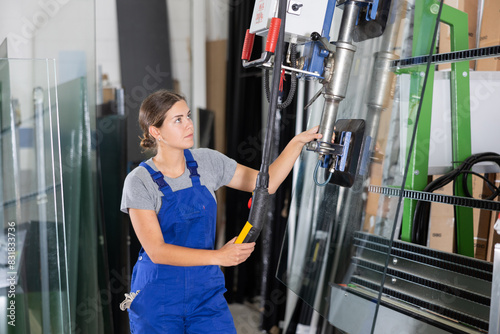 Female worker using control panel and lifting mechanism controls the movement of window panes in an industrial workshop