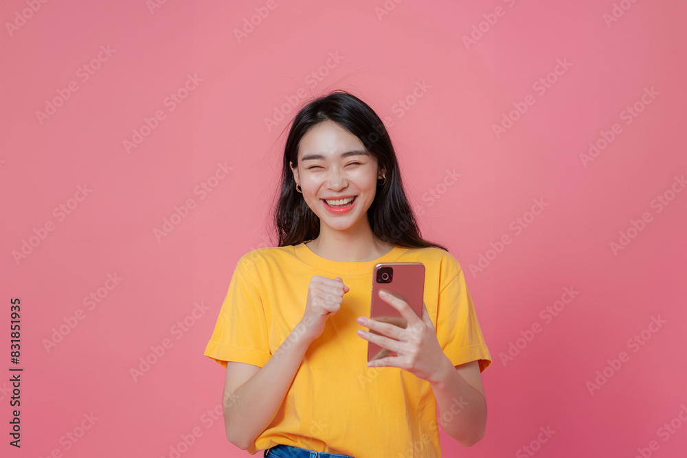 Smiling Young Woman in Yellow T-Shirt Holding Smartphone and Celebrating with Fist Pump on Pink Background - Generative AI Smiling Young Woman in Yellow T-Shirt Holding Smartphone and Celebrating with Fist Pump on Pink Background - Generative AI