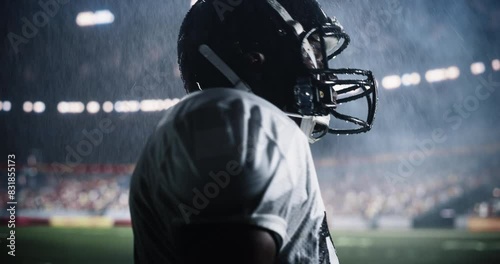 Portrait of a Focused American Football Player Standing Outdoors in a Stadium Under Heavy Rain. Raindrops Sliding Down His Helmet. African Man is Unfazed, Concentrated on the Championship Game photo