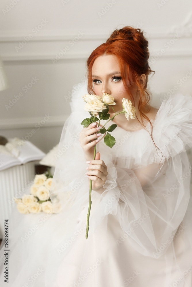 Beautiful redhead girl in white dress holds white roses in her hands and enjoys the smell of flowers. Beautiful redhead girl in white dress holds white roses in her hands and enjoys the smell of flowers.