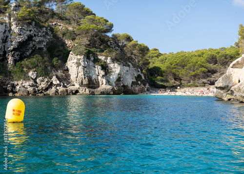 View of Macarelleta cove in the south of the island of Menorca, seen from the water with unrecognizable people sunbathing and a warning buoy in the foreground photo
