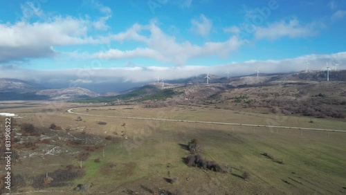 Beautiful aerial shot of Croatian landscape with wind turbines generating renewable energy in the background and an empty road, in the region of Lika in Croatia, Europe (ID: 831908522)