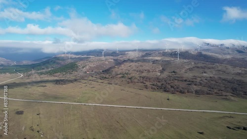 Beautiful aerial shot of Croatian landscape with wind turbines generating renewable energy in the background and an empty road, in the region of Lika in Croatia, Europe (ID: 831917188)