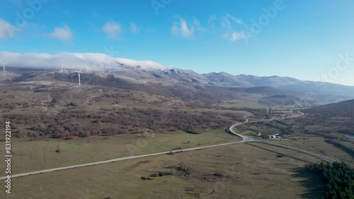 Beautiful aerial shot of Croatian landscape with wind turbines generating renewable energy in the background and an empty road, in the region of Lika in Croatia, Europe (ID: 831922194)
