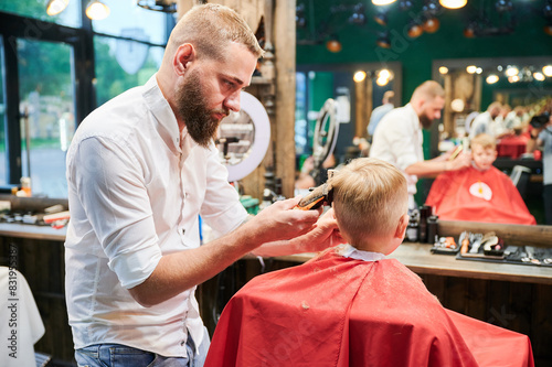 Barber using comb and shaver to cut hair. Professional hairdresser shaving little kid's nape. photo