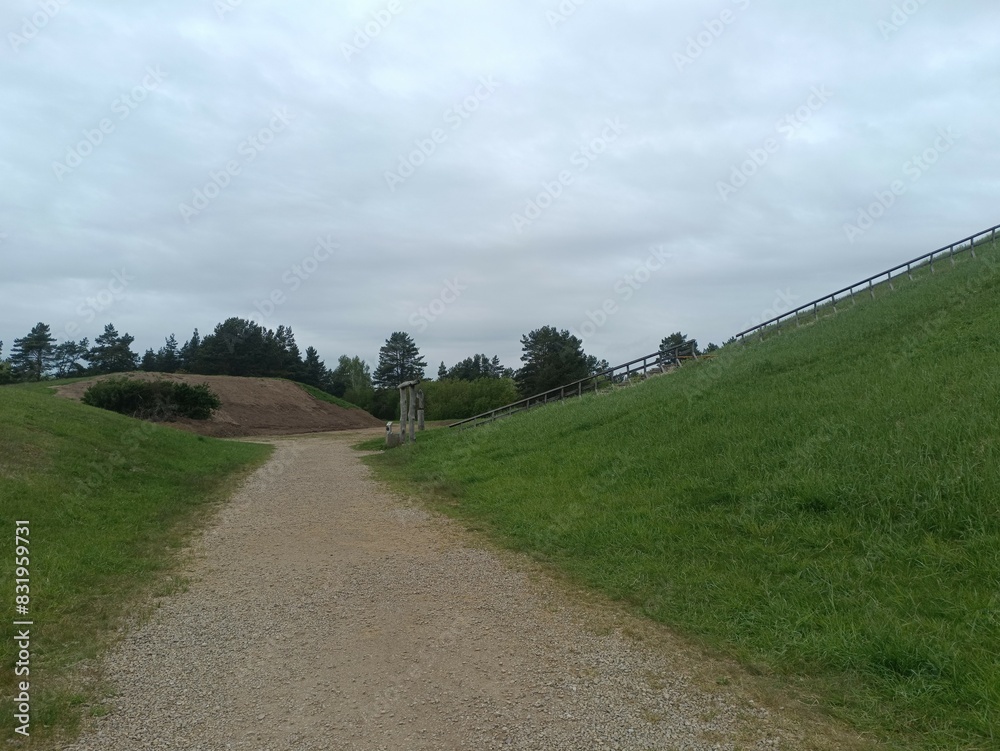 Salduve hill during cloudy day. Small hill. Grass is growing on hill. Staircase leading to the top. Cloudy day with white and gray clouds in sky. Nature. Salduves piliakalnis. Salduve hill during cloudy day. Small hill. Grass is growing on hill. Staircase leading to the top. Cloudy day with white and gray clouds in sky. Nature. Salduves piliakalnis.