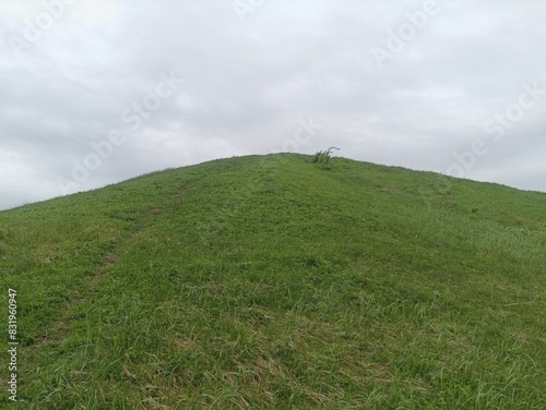 Salduve hill during cloudy day. Small hill. Grass is growing on hill. Staircase leading to the top. Cloudy day with white and gray clouds in sky. Nature. Salduves piliakalnis.