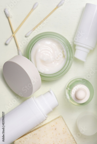 Opened cream jar with balnk lid near cosmetic products on light yellow top view, mockup
