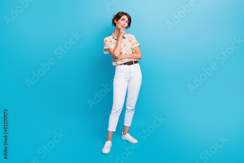 Full size portrait of minded doubtful girl arm touch chin look interested empty space isolated on blue color background © deagreez