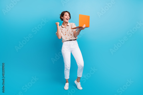 Full size portrait of glad positive girl use laptop raise fist shout yes hooray achievement isolated on blue color background photo