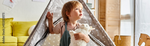 Fotografia Adorable curly-haired toddler girl cuddling her soft toy inside a teepee