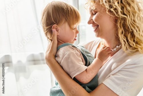 A curly mother lovingly cradling her toddler daughter in her arms at home.