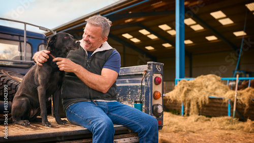 Canvas Print Mature Male Farm Worker Sitting On Tailgate Of Off Road Farm Vehicle With Dog