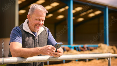 Mature Male Farm Worker Standing Outside Barn Checking Mobile Phone photo