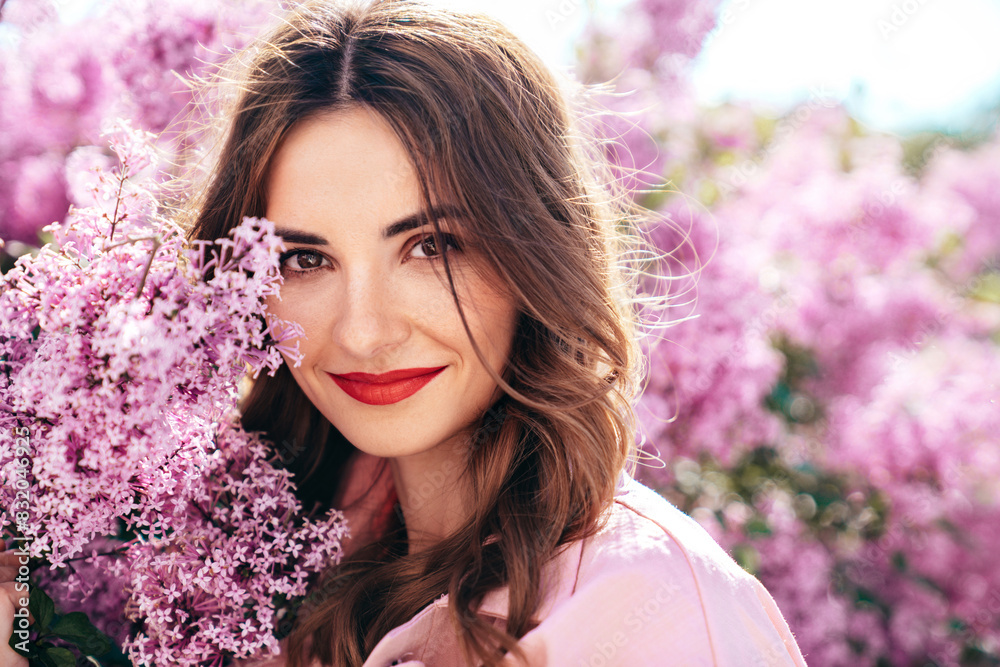 Young beautiful smiling woman. Sexy carefree model posing in the street. Positive model near blooming flower lilac bush beaming. Summertime, pink colours. Closeup beauty portrait, red lips Young beautiful smiling woman. Sexy carefree model posing in the street. Positive model near blooming flower lilac bush beaming. Summertime, pink colours. Closeup beauty portrait, red lips