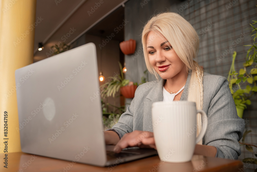 A woman is sitting at a table with a laptop and a white coffee cup. She is smiling and she is enjoying her time. A woman is sitting at a table with a laptop and a white coffee cup. She is smiling and she is enjoying her time.