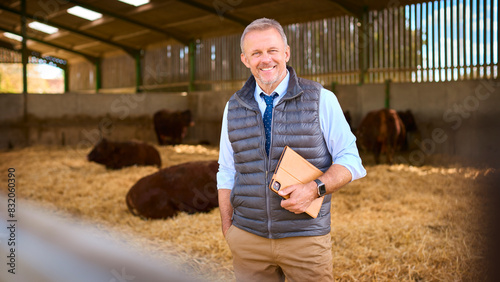 Bild auf Leinwand Portrait Of Mature Male Farm Worker Or Manager Standing Inside Cattle Barn With