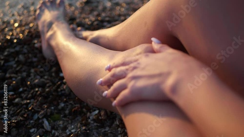 Woman with beautiful legs sitting on pebble beach by sea, closeup. Camera moving after her hand