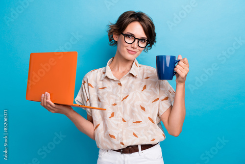 Portrait of successful pretty girl hold laptop fresh coffee mug isolated on blue color background photo