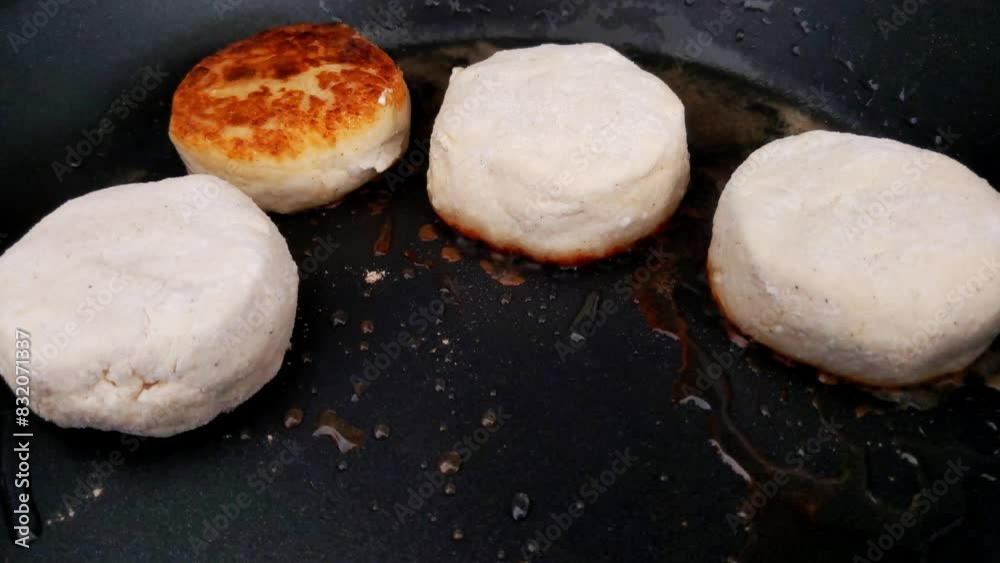 Close-up view of four biscuits being cooked in a hot pan, with one biscuit showing a golden-brown top while the others are still white. the scene highlights the process of home baking, emphasizing fre