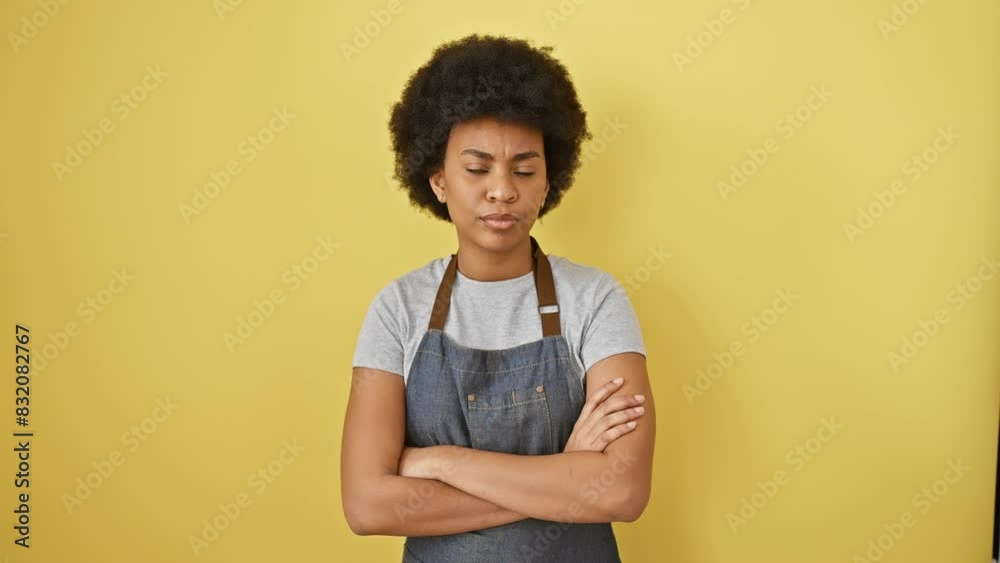 Disapproving african american woman, nervous skeptic, sporting apron, cross-armed, negative vibes over yellow isolated background Disapproving african american woman, nervous skeptic, sporting apron, cross-armed, negative vibes over yellow isolated background