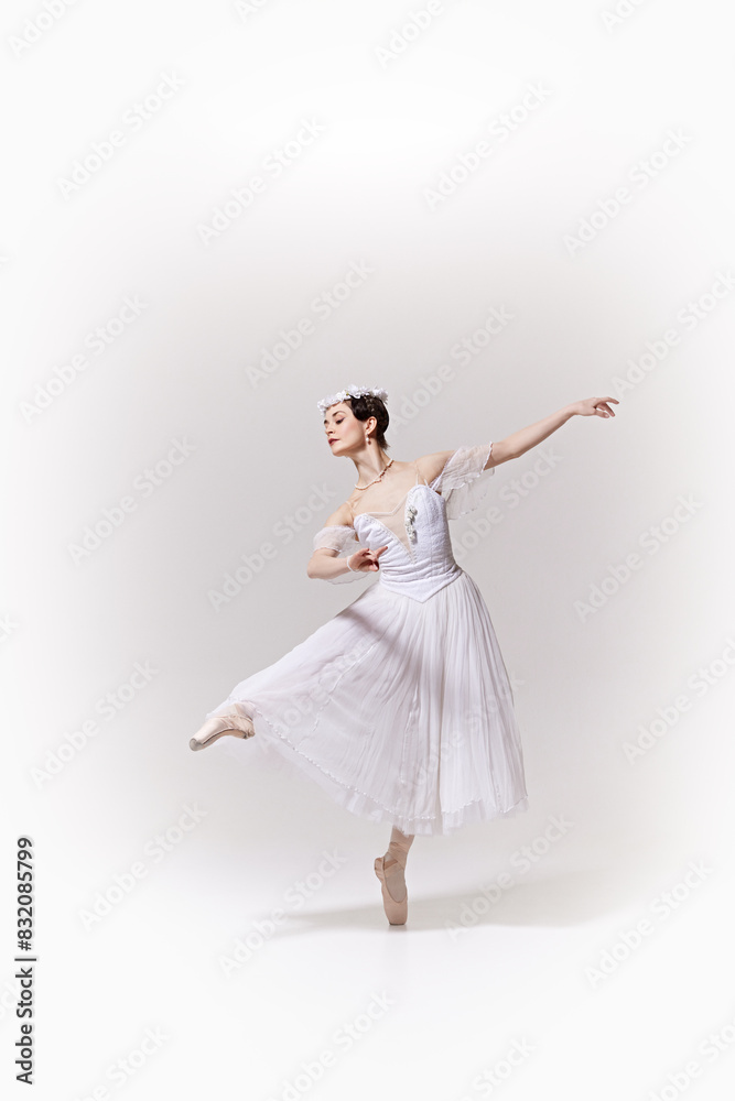 Beautiful ballerina in white dress, performing exquisite ballet move on pointe against white studio background. Concept of art, fusion of classic and modernity, grace and elegance. Beautiful ballerina in white dress, performing exquisite ballet move on pointe against white studio background. Concept of art, fusion of classic and modernity, grace and elegance.