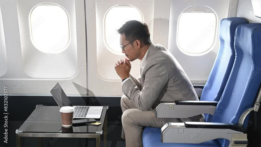 Photo of a frustrated man sitting on an airplane with her head in her hands. Asian Businessman sitting in airplane working laptop and tablet Photo of a frustrated man sitting on an airplane with her head in her hands. Asian Businessman sitting in airplane working laptop and tablet
