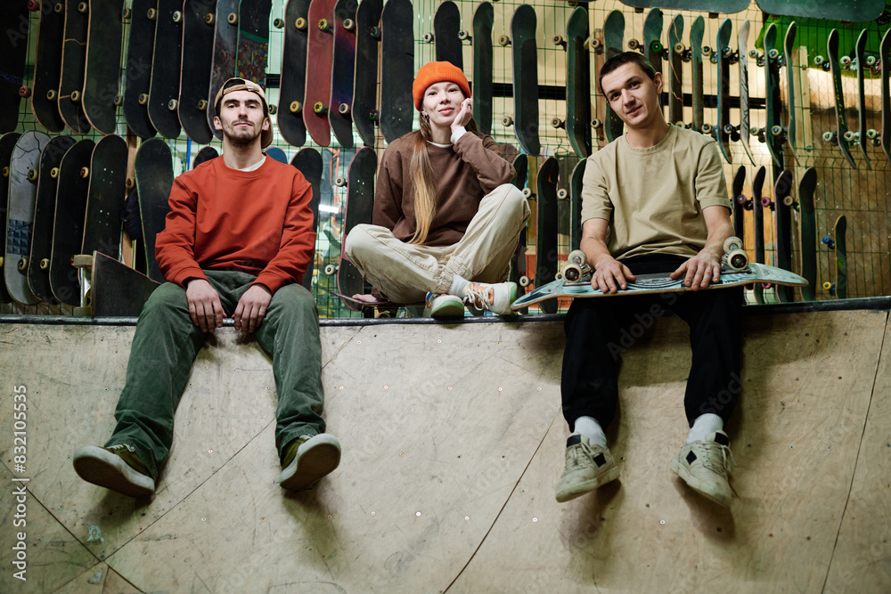 Group of self-confident young male and female skateboard riders in streetwear sitting relaxed in skatepark and looking at camera Group of self-confident young male and female skateboard riders in streetwear sitting relaxed in skatepark and looking at camera