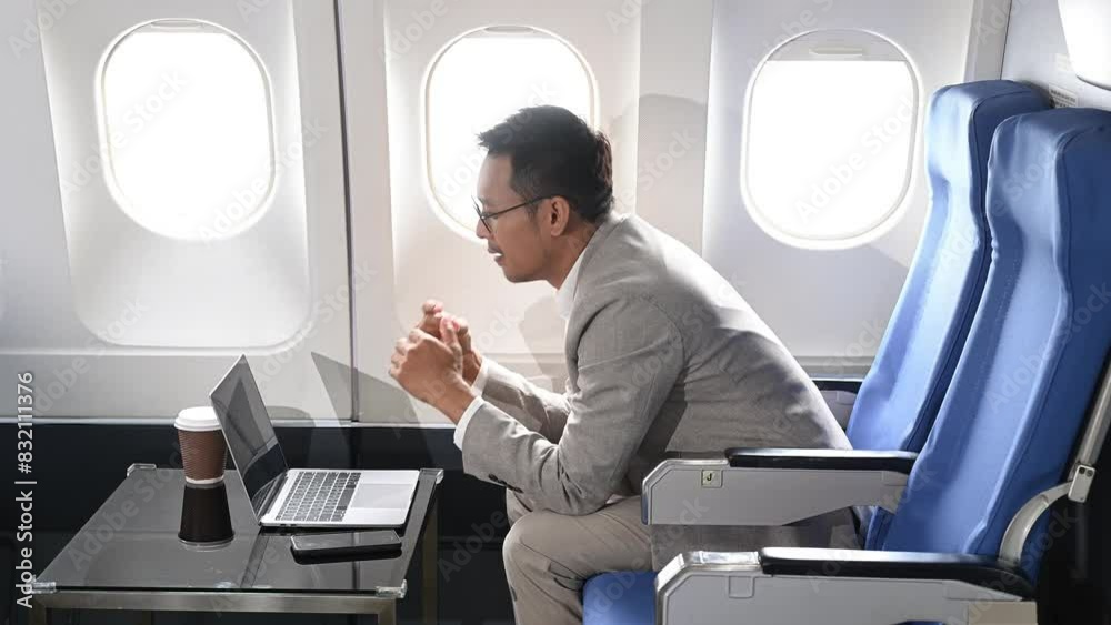 Attractive Asian male passenger of airplane sitting in comfortable seat while working laptop and tablet with mock up area using wireless connection. Attractive Asian male passenger of airplane sitting in comfortable seat while working laptop and tablet with mock up area using wireless connection.