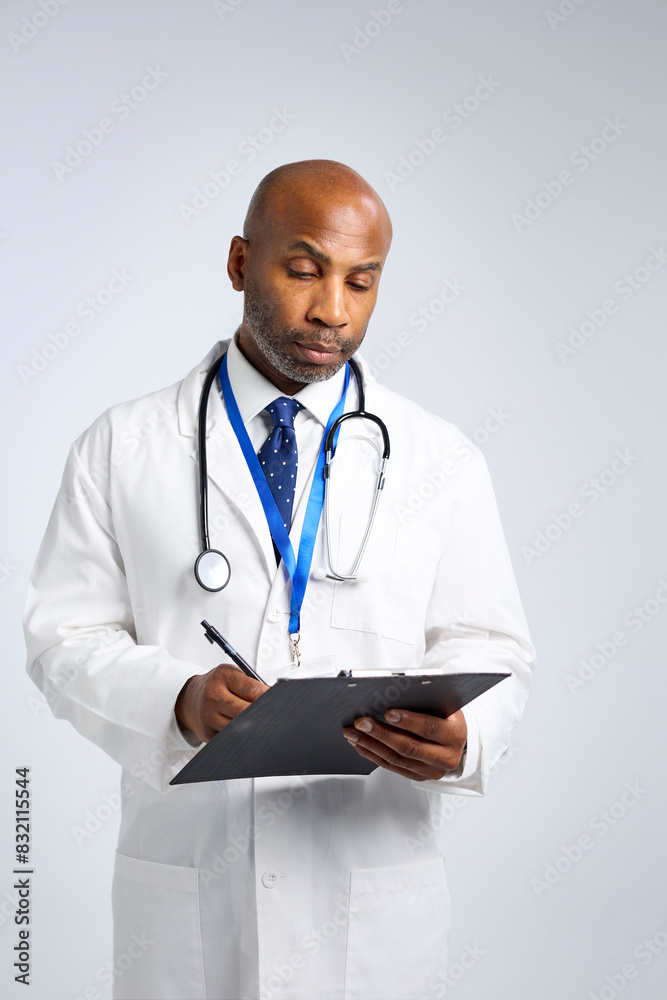 Fototapeta premium Studio Portrait Of Mature Doctor Wearing White Coat Writing On Patient Chart On Clipboard