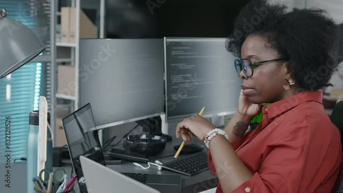 Side view chest up of Black female office employee looking at laptop screen with program codes on it