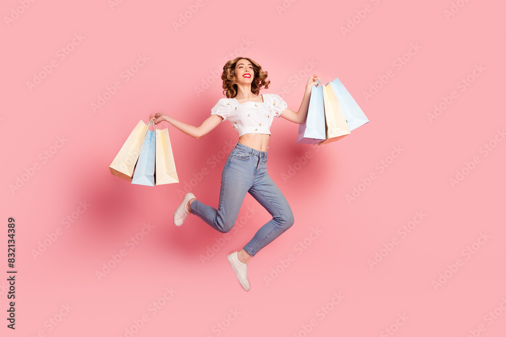 Full size photo of pretty woman dressed white blouse jeans holding shopping bags fly look empty space isolated on pink color background Full size photo of pretty woman dressed white blouse jeans holding shopping bags fly look empty space isolated on pink color background